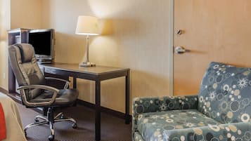 A hotel room with a desk, chair, TV, lamp, and a patterned sofa.
