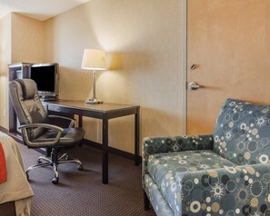 A hotel room with a desk, chair, TV, lamp, and a patterned sofa. - Comfort Inn On the Bay (Port Orchard)