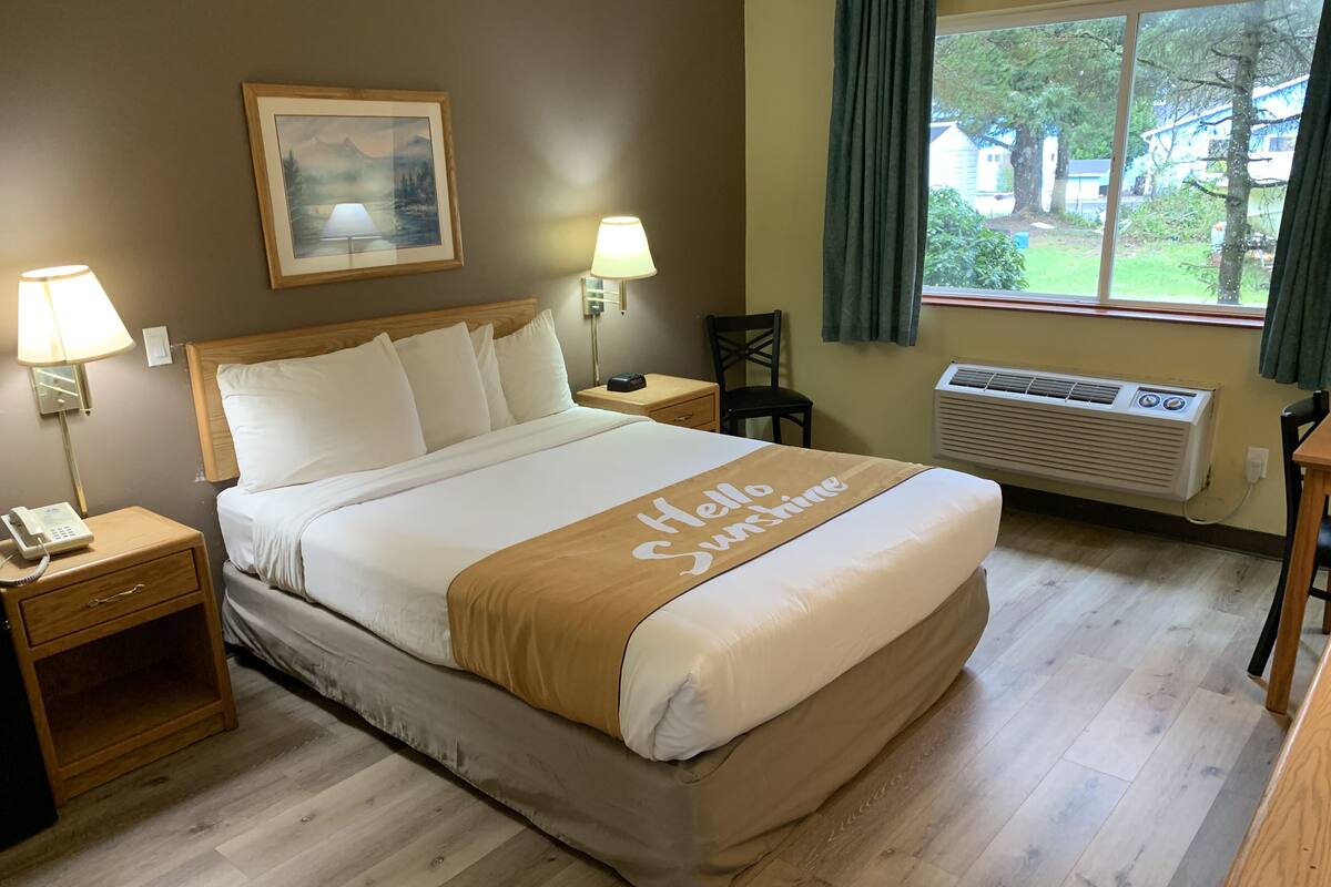 Habitación de hotel con cama, lámparas de noche, un cuadro enmarcado en la pared, ventana con cortinas y un equipo de aire acondicionado.