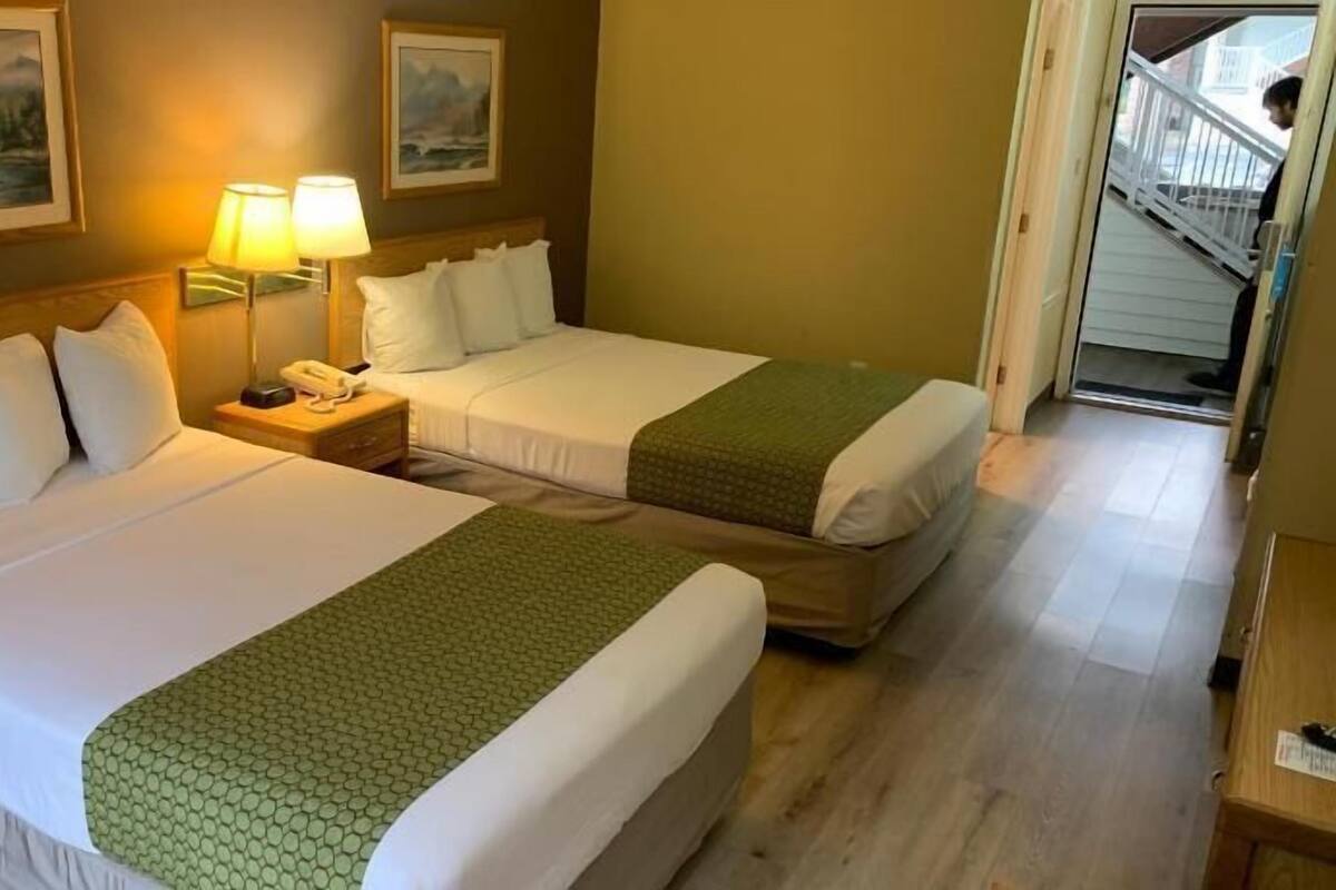 Una habitación de hotel con dos camas, una mesita de noche con teléfono y dos lámparas de pared.