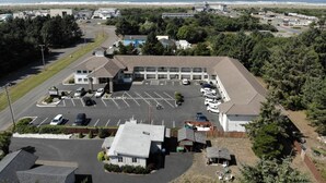 An aerial view of a building with a parking lot, surrounded by greenery and a beach in the background. - Days Inn by Wyndham Ocean Shores (Ocean Shores)