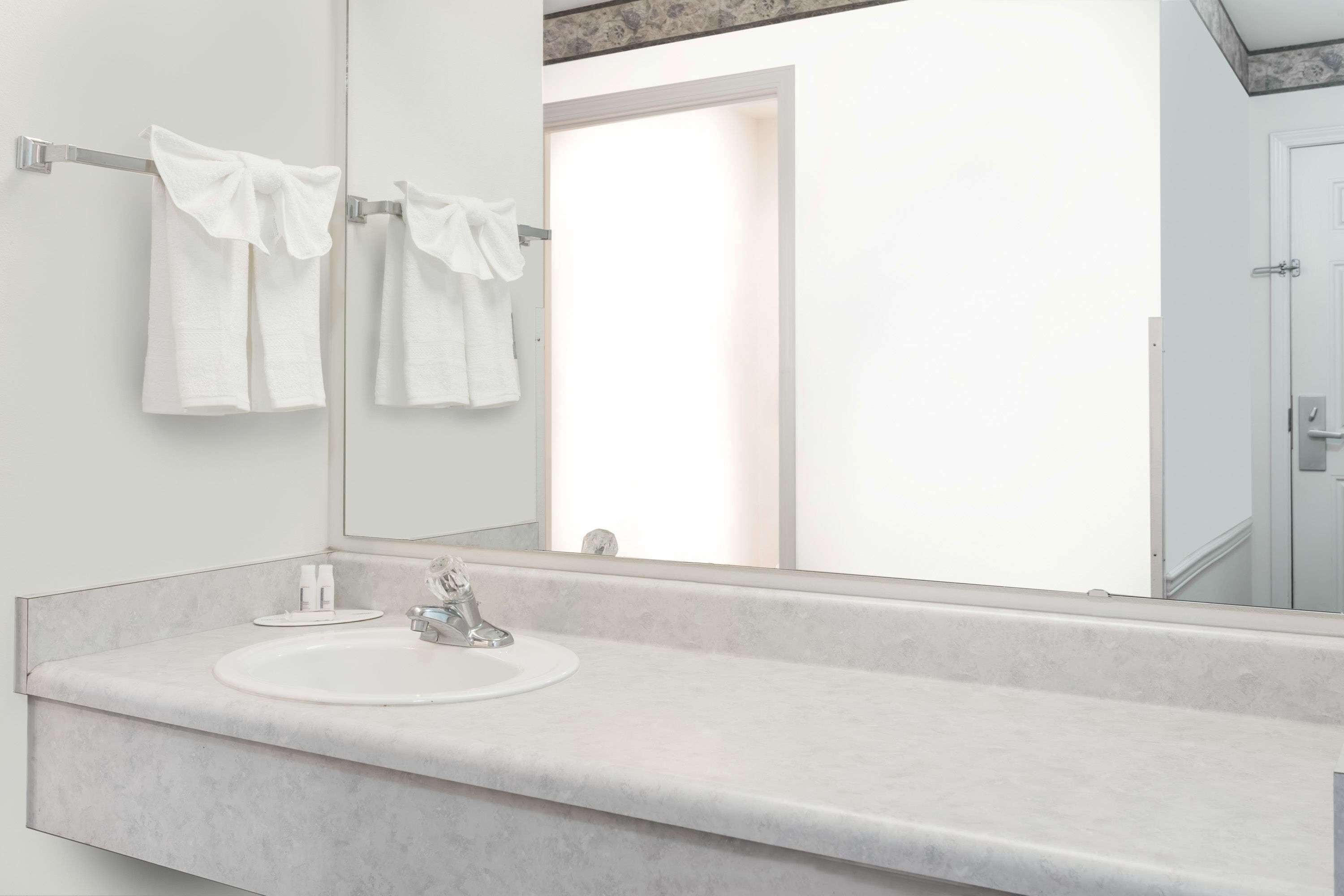 A modern bathroom with a large mirror, a white sink, and two towels hanging on a towel rack.