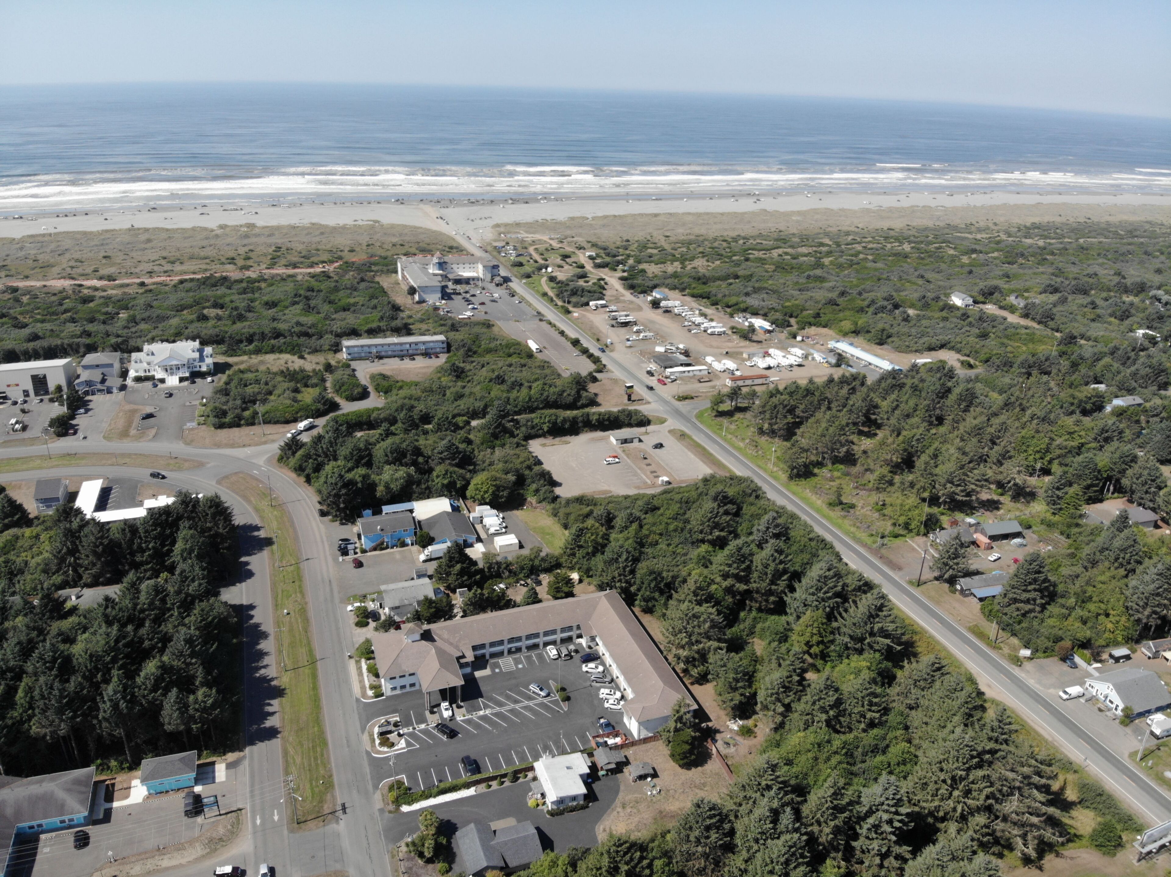 An aerial view of a coastal area with a parking lot, buildings, and a beach.