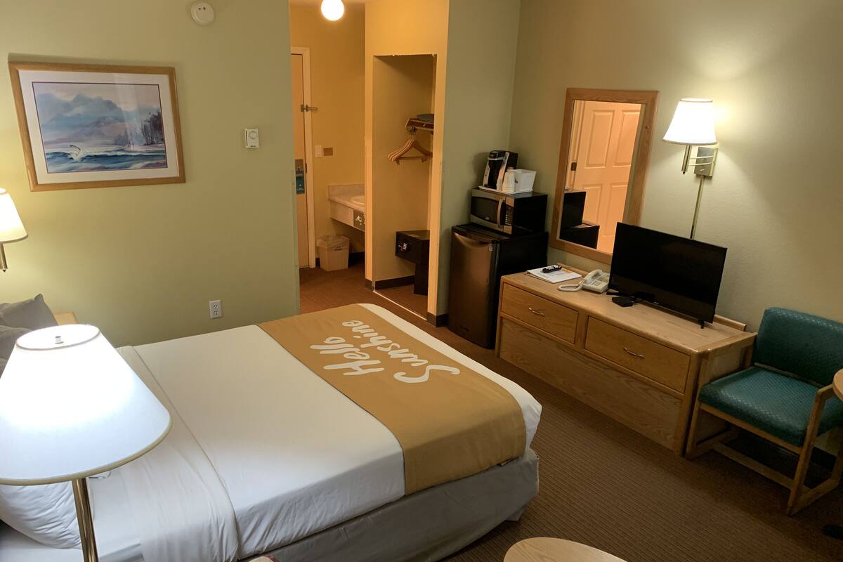 Habitación de hotel con cama, escritorio con computadora, televisor, silla y baño a la vista.