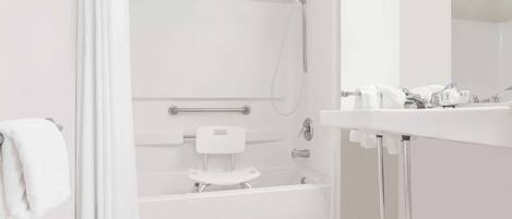 A modern bathroom with a walk-in shower, a toilet with a safety rail, and a sink with a mirror.