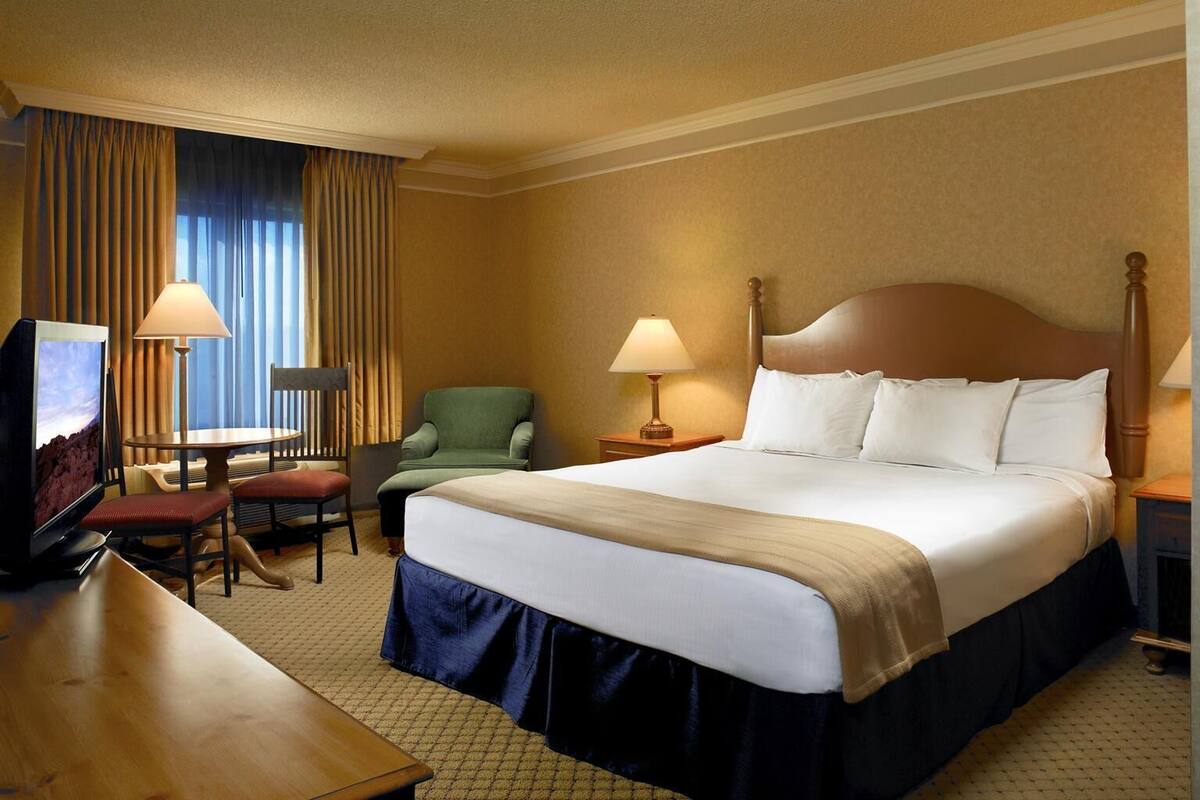 A hotel room with a bed, a desk, a chair, a TV, and two lamps.
