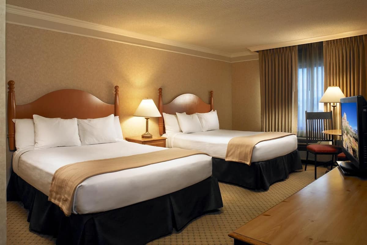 A hotel room with two beds, a desk, a chair, and a TV.