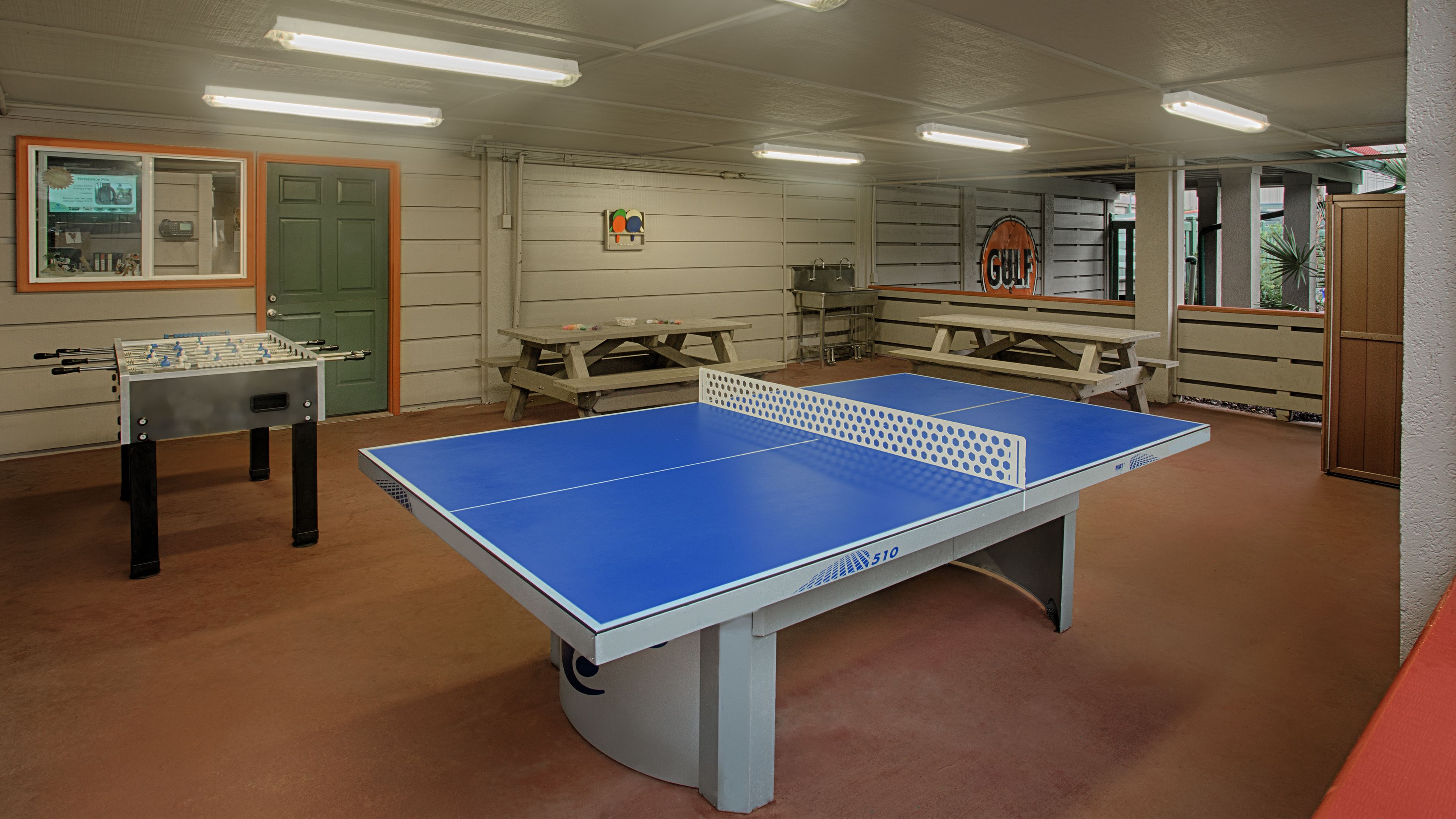 Ein Raum mit einem Tischtennisch, einem Kicker und Picknicktischen.