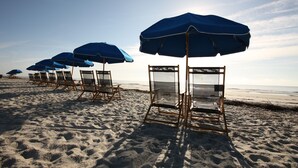 Des chaises de plage et des parasols sont alignés sur une plage de sable.