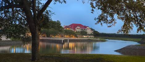 A lakeside property with a large building featuring a red roof, surrounded by trees and a calm lake.