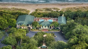Vue aérienne d’un complexe hôtelier doté d’une piscine, entouré d’une végétation luxuriante et avec une plage en arrière-plan.