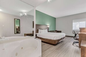 Een moderne hotelkamer met een groot, wit bad, een bed met wit beddengoed, een bureau met stoel en een spiegel aan de muur.