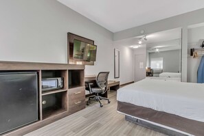 Une chambre d’hôtel équipée d’un lit, d’un bureau avec une chaise, d’une télévision et d’un four à micro-ondes.