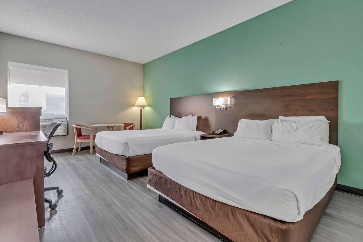Une chambre d’hôtel avec deux lits, un bureau, une chaise, une lampe et une fenêtre.