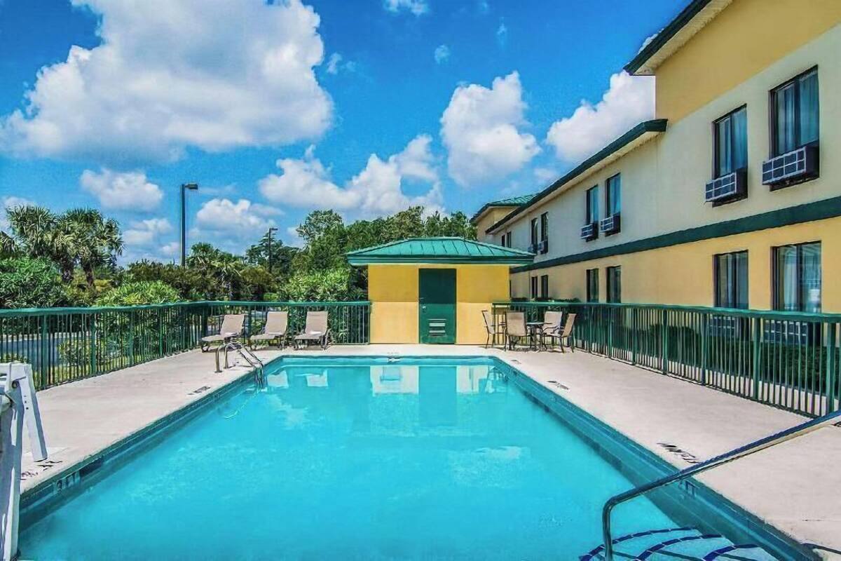 Une piscine avec des chaises longues, un petit bâtiment doté d’un toit v égétalisé et un bâtiment jaune avec des fenêtres.