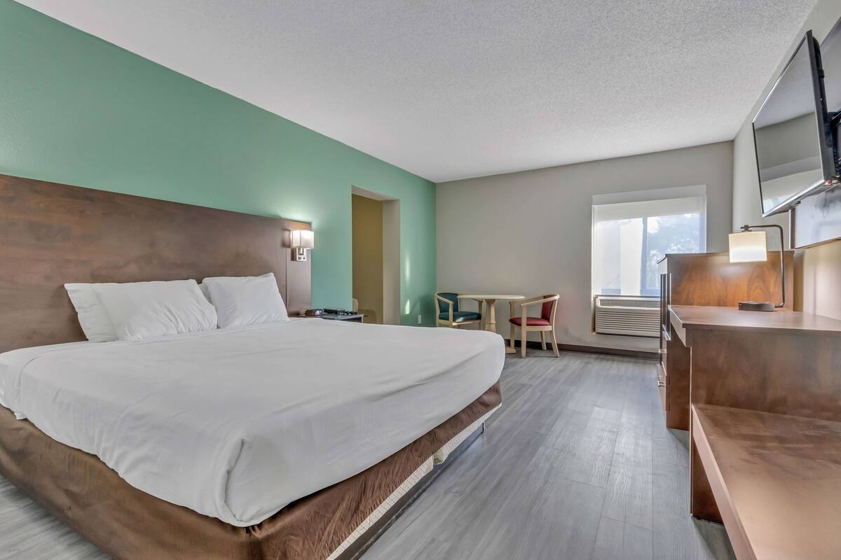Une chambre d’hôtel avec un grand lit, un bureau, une chaise, une petite table, un téléviseur et une fenêtre.