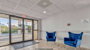 A lobby with two blue armchairs, a fire alarm, and exit signs. - Baymont by Wyndham N Myrtle Beach/Park & Sports Complex Area (North Myrtle Beach)