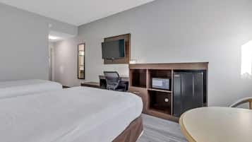 A hotel room with two beds, a desk, a chair, a TV, and a refrigerator.
