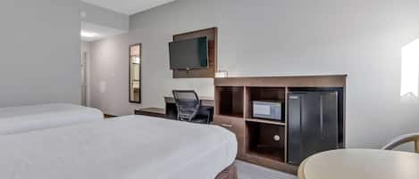A hotel room with two beds, a desk, a chair, a TV, and a refrigerator.