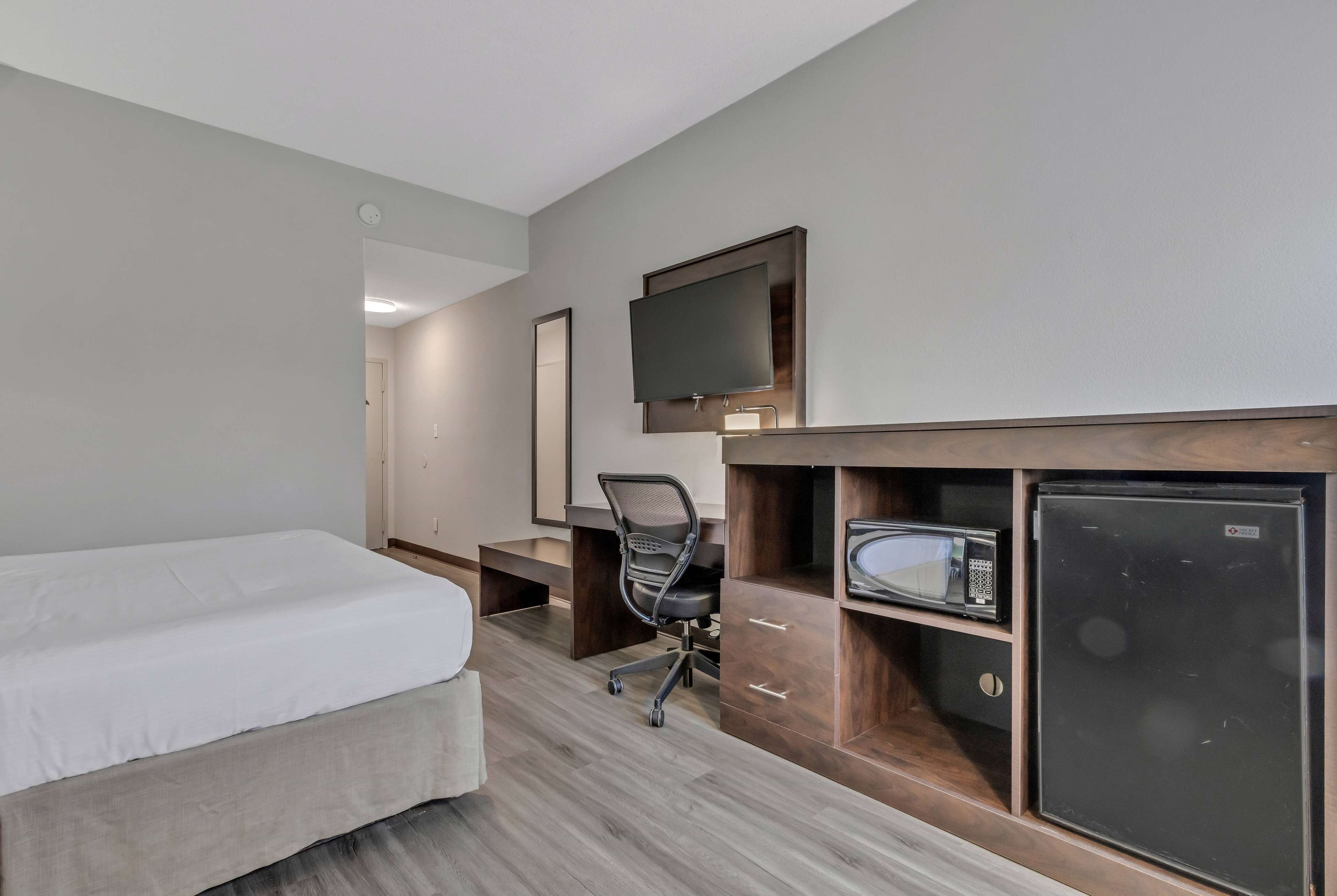 A hotel room with a bed, a desk with a chair, a television, a microwave, and a refrigerator.