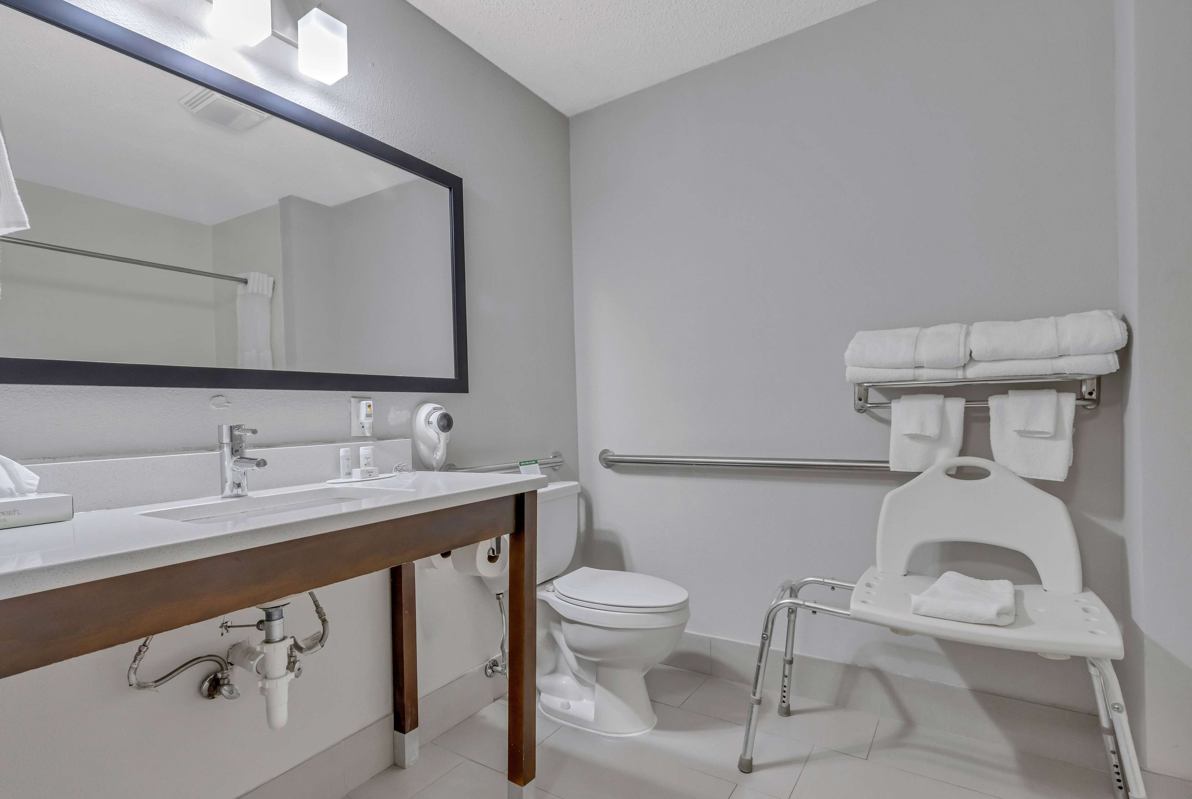 Un baño moderno con lavamanos, espejo, inodoro y barra de apoyo.