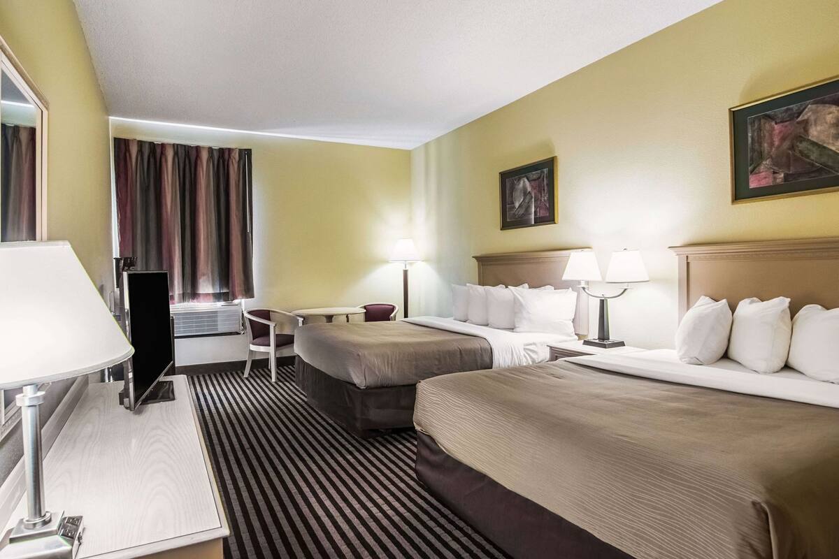 Une chambre d’hôtel avec deux lits, un bureau, une chaise, un téléviseur à écran plat et un tableau au mur.