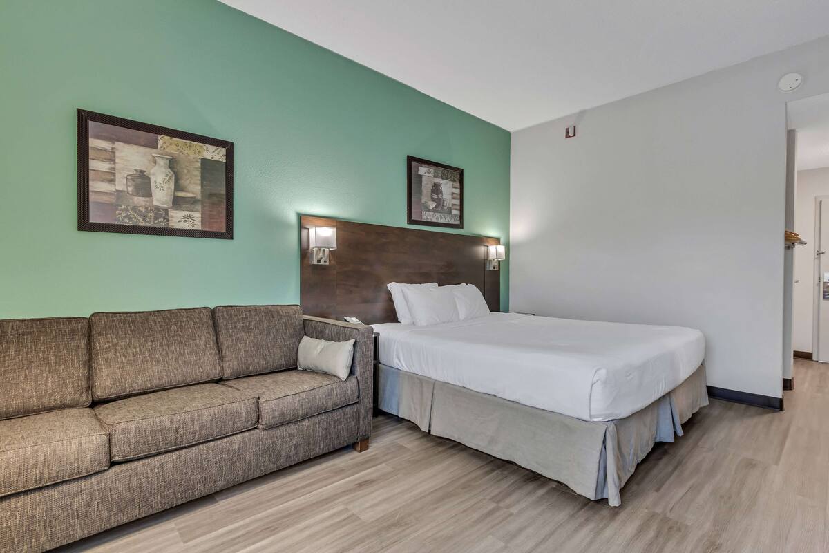 Une chambre d’hôtel avec un lit, un canapé, deux lampes fixées au mur et deux tableaux encadrés accrochés au mur.