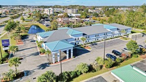A hotel with a blue roof, a covered outdoor area, and a parking lot. - Baymont by Wyndham N Myrtle Beach/Park & Sports Complex Area (North Myrtle Beach)