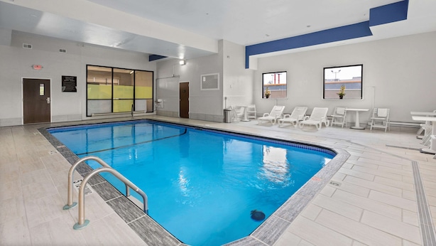 An indoor swimming pool with clear lanes, a lifeguard chair, and a sunlit area with chairs and tables. - Comfort Inn & Suites Hazelwood - St. Louis (Hazelwood)