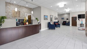 A reception area with a stone wall, a reception desk, and a seating area with blue chairs. - Comfort Inn & Suites Hazelwood - St. Louis (Hazelwood)