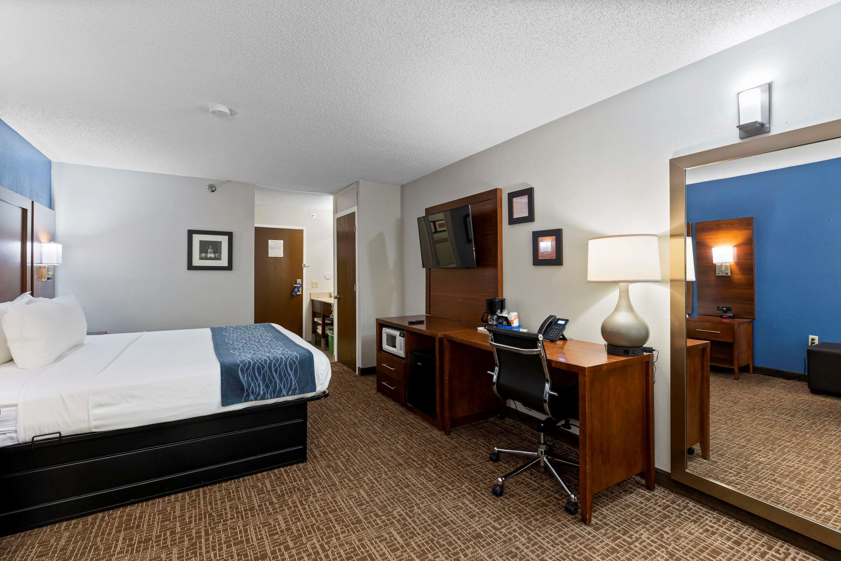 A hotel room with a bed, desk, chair, and a large mirror.