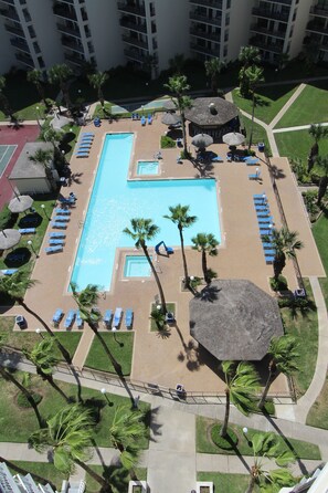 En vy från ovan över ett hotells poolområde med flera pooler, solstolar, palmer och en central paviljong.