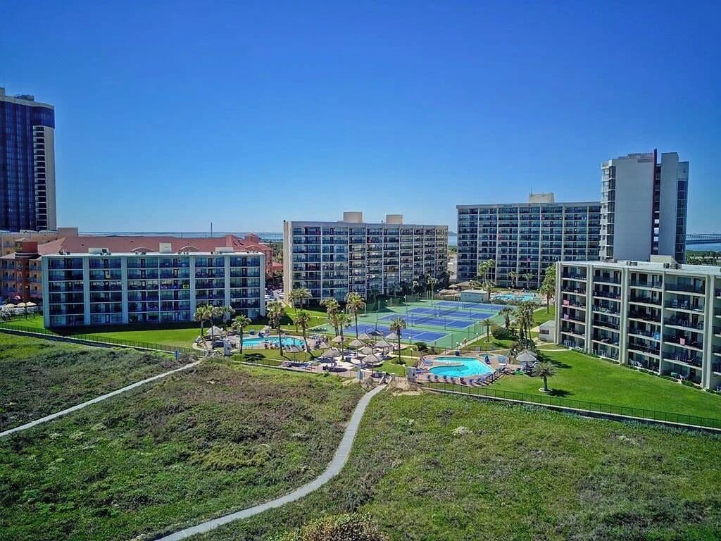 A modern hotel complex with multiple high-rise buildings, a central courtyard with a pool, and a well-maintained lawn.