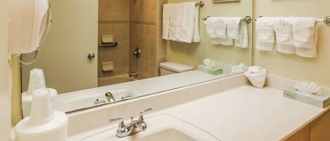 Une salle de bain avec un grand lavabo, un miroir, une douche et plusieurs serviettes blanches disposées sur un porte-serviettes.