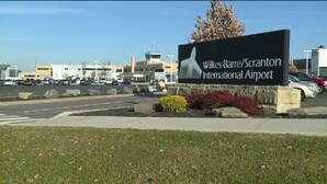 Ein Flughafenschild mit dem Text "Wilkes-Barre/Scranton International Airport" und Blick auf das Terminal sowie den Parkplatz.