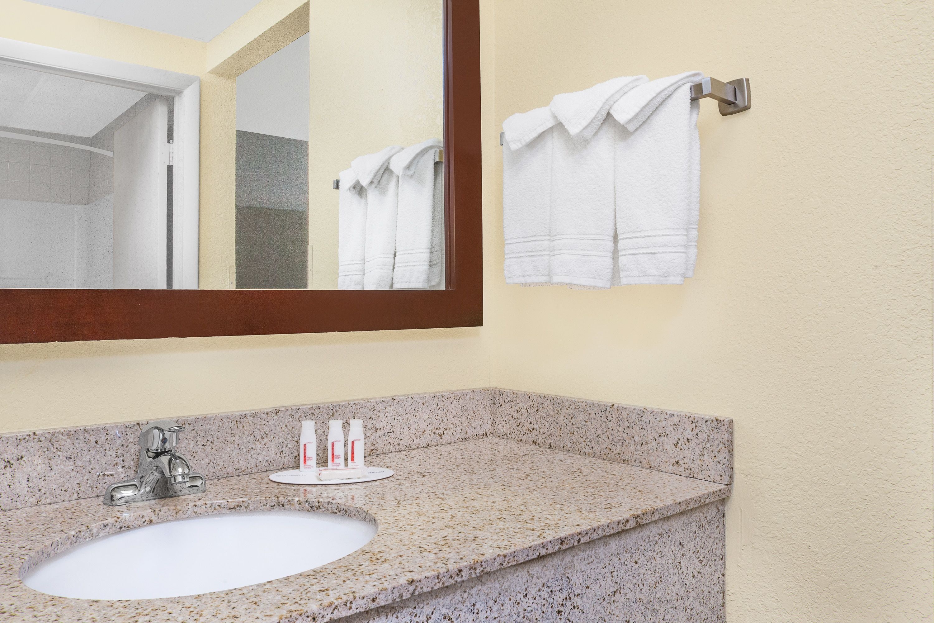 A bathroom with a granite countertop sink, a mirror, and two towels hanging on a towel rack.