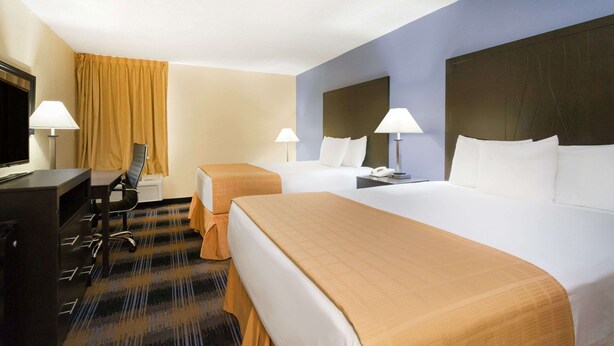Ein Hotelzimmer mit zwei Betten, einem Schreibtisch, einem Stuhl, einem Fernseher und Lampen.