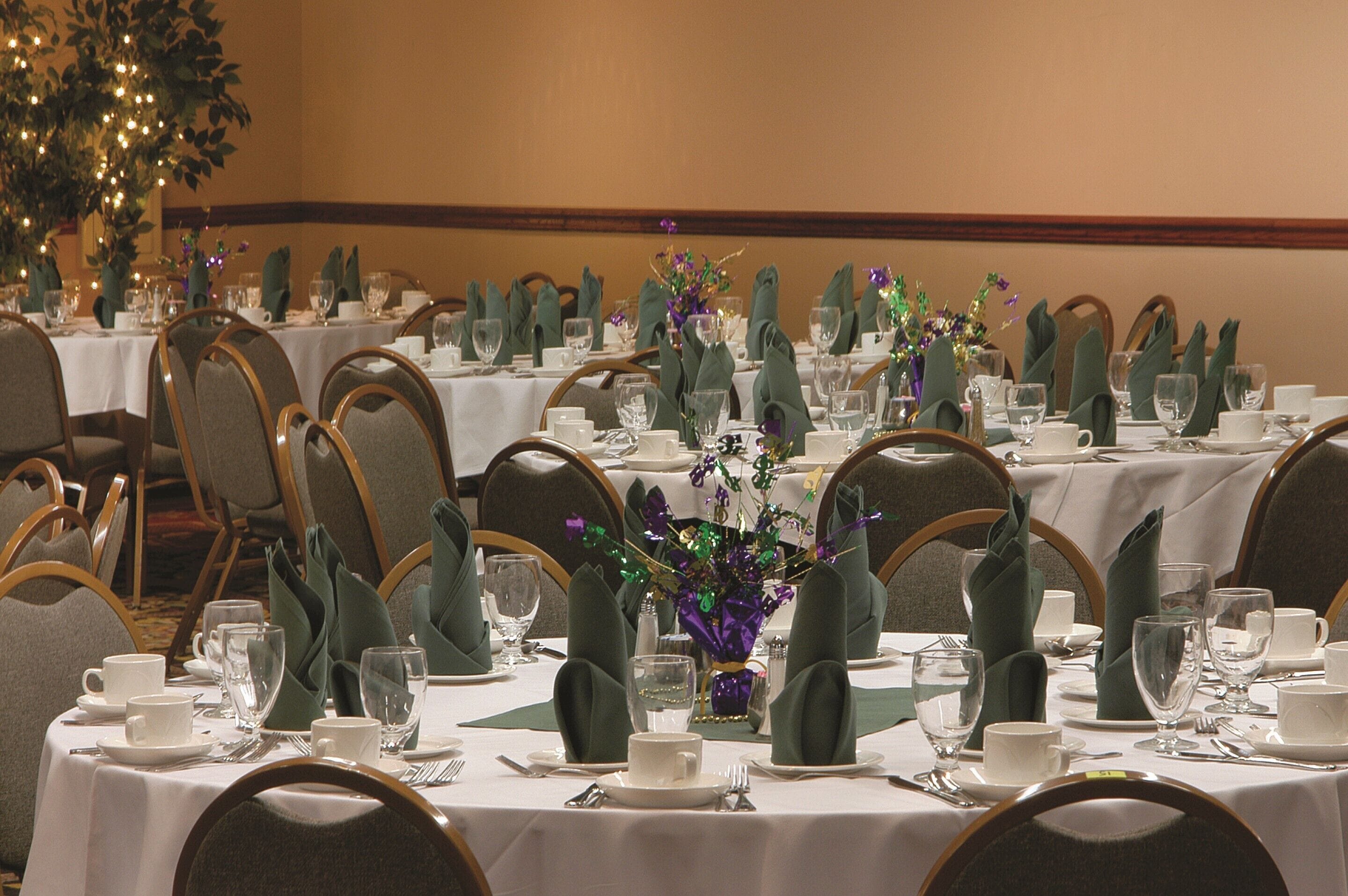 A banquet hall with multiple tables set for dining, each with chairs, plates, cutlery, and glassware.