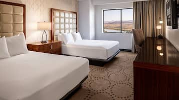 Habitación de hotel con dos camas, un escritorio, televisor y ventana grande con vistas.