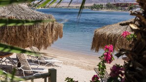 A beach with thatched umbrellas and lounge chairs, a calm sea, and distant mountains.