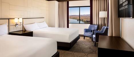 A hotel room with two beds, a desk, a TV, and a view of a lake.