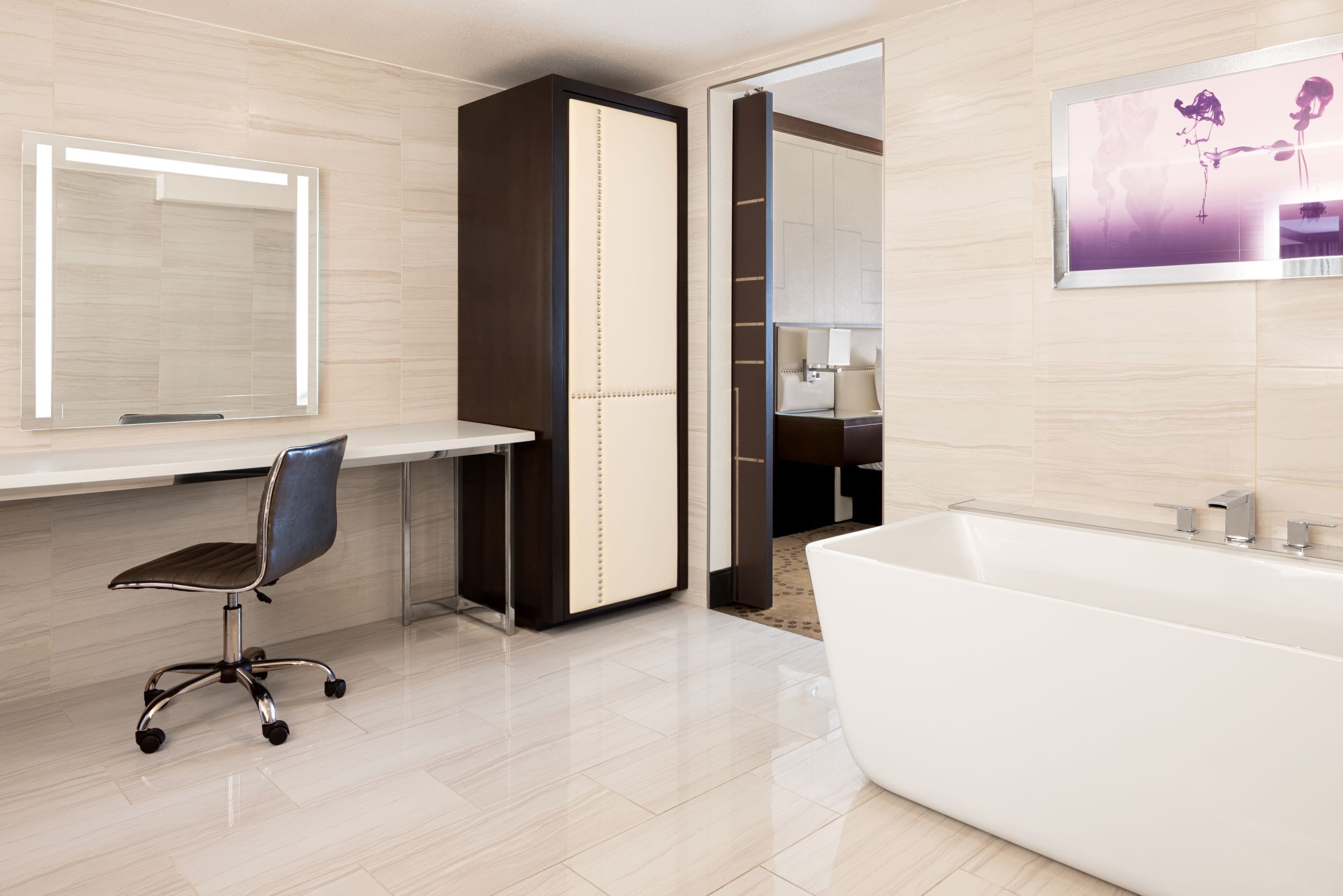 A modern bathroom with a large mirror, a white bathtub, and a desk with a chair.