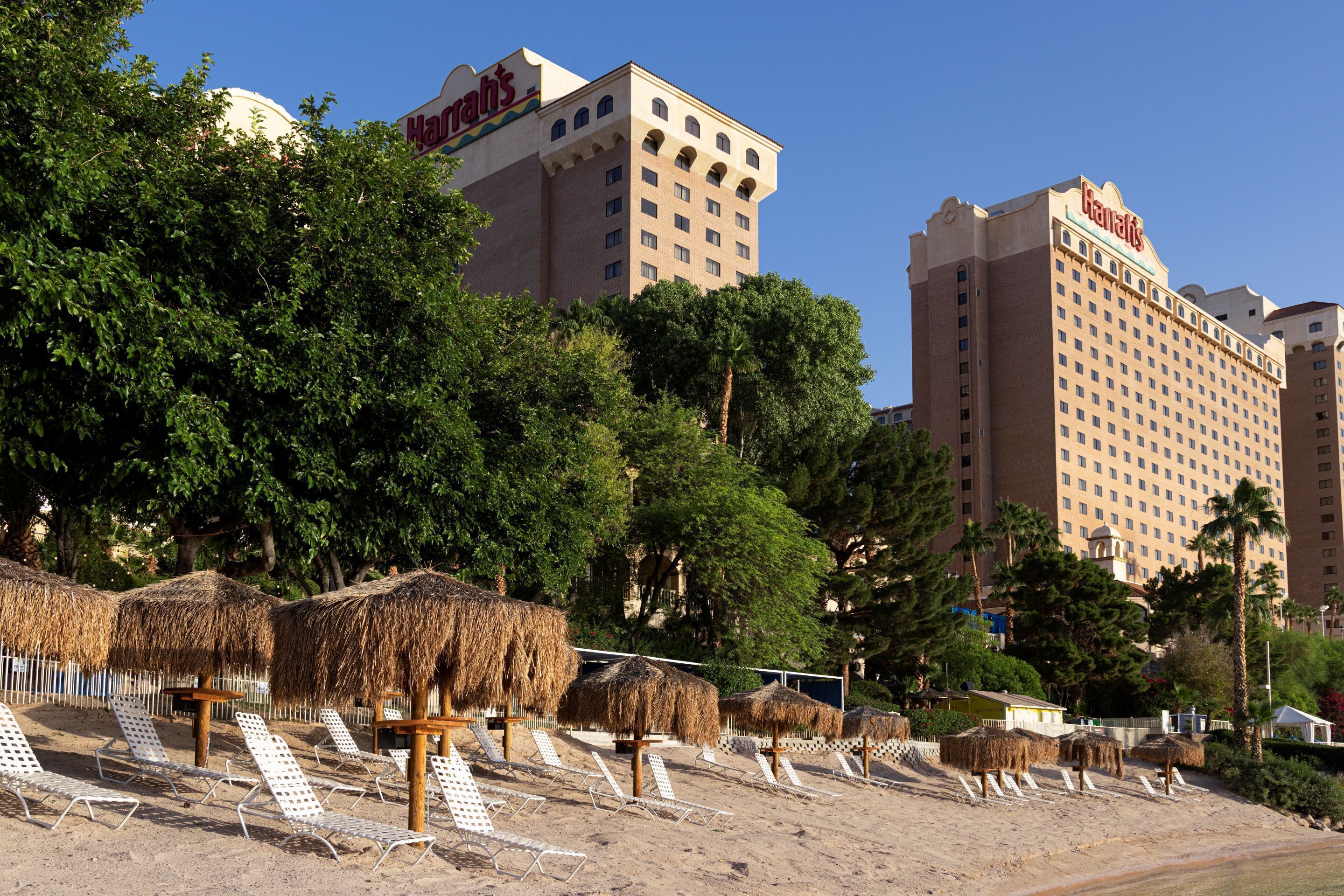 Un hotel de varios pisos, con palmeras y sombrillas de paja en la playa.