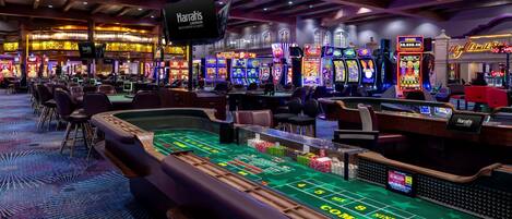 A casino floor with multiple slot machines, a craps table, and a Harrah's sign.