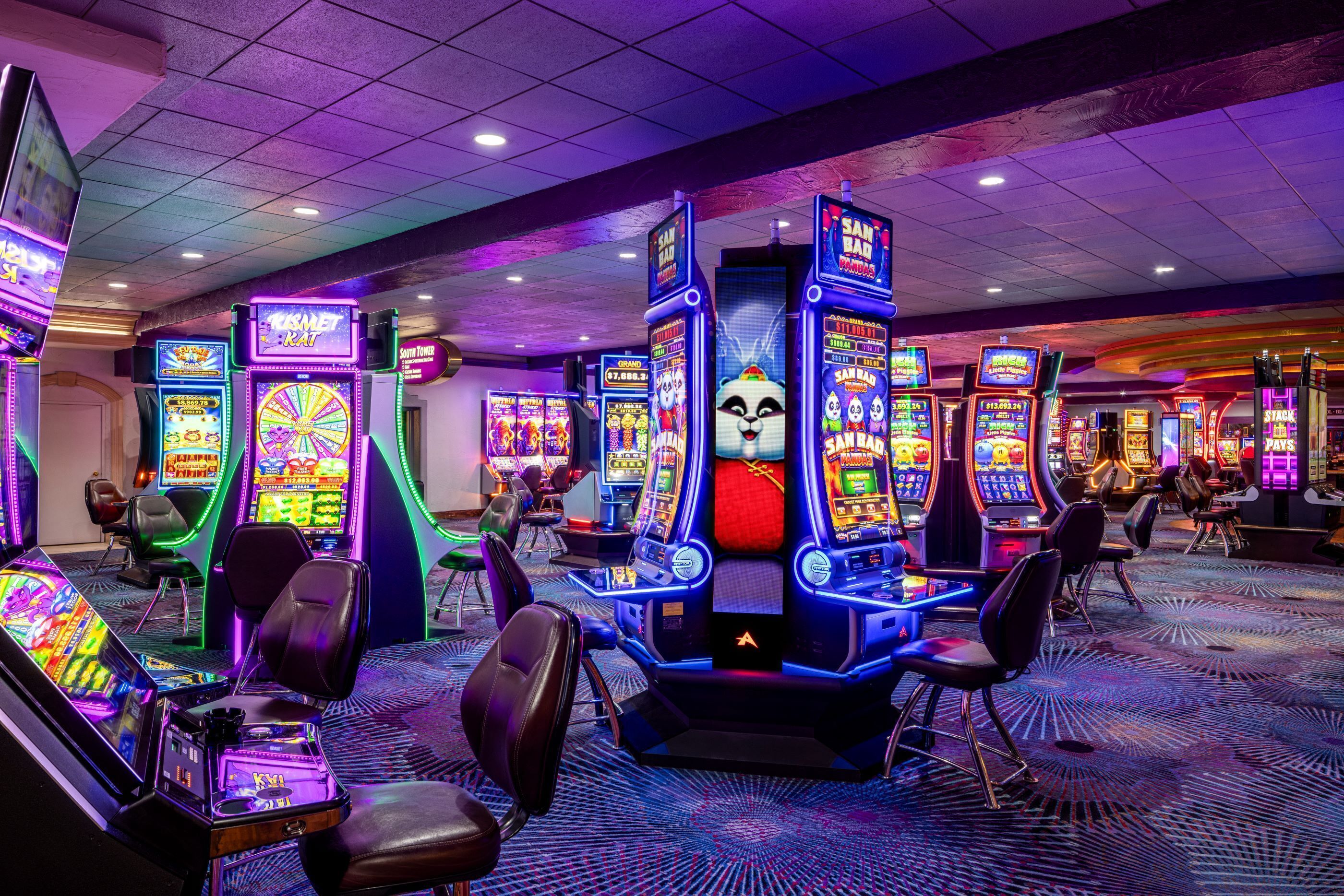 A casino with various slot machines and gaming tables, featuring vibrant neon lights and a carpeted floor.
