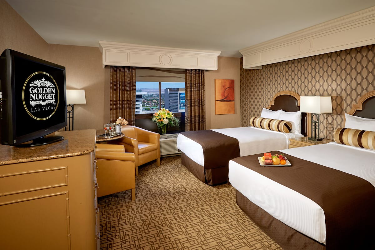 Quarto de hotel com duas camas, televisão, escrivaninha e vista para a cidade.