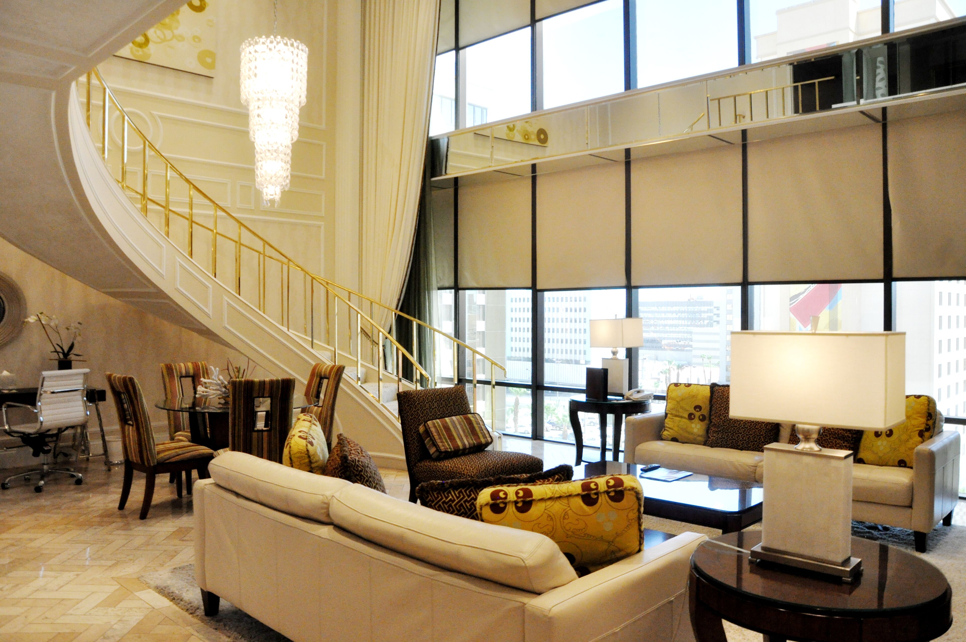 A spacious living area with a curved staircase, comfortable seating, and large windows offering city views.