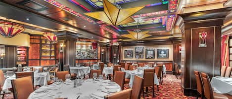 A restaurant with round tables, brown leather chairs, and a colorful stained glass ceiling.