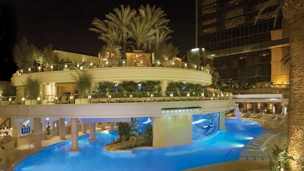 A hotel with a large indoor pool, palm trees, and a modern building in the background.