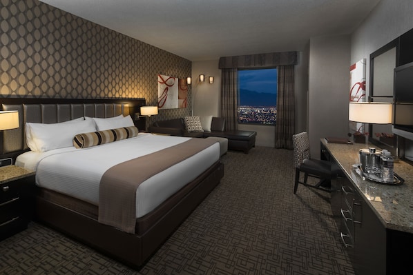 Habitación de hotel con una cama grande, un escritorio, una silla y vista a la ciudad de noche.